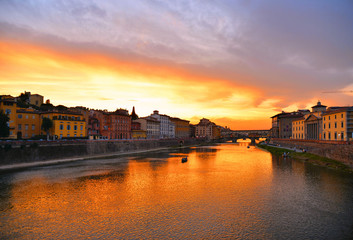 Fototapeta premium colorful buildings, bridge Ponte Vecchio and water reflections in warm sunset on river Arno with small boats in florence, italy