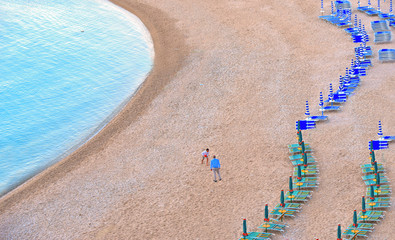Father and son playing on empty beach with turquoise water, blue and green umbrellas and chaise...
