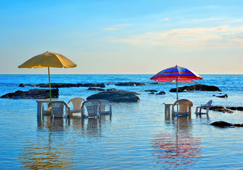 Tables and chairs immersed in the sea water under colorful umbrellas with the background of sea horizon, Agrigento Italy