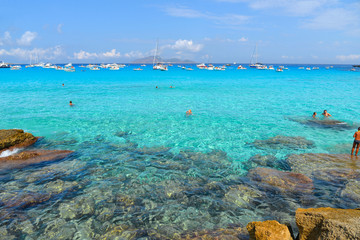 people inside paradise clear torquoise blue water with boats and cloudy blue sky in background in Favignana island, Cala Rossa Beach, Sicily South Italy.