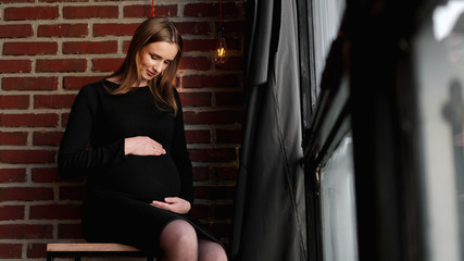 Fototapeta na wymiar Young pretty pregnant woman in black dress in studio - loft interior