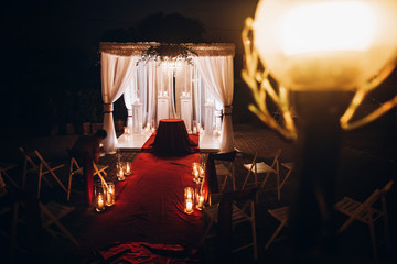wedding venue aisle with candles in glass lanterns and arch, stylish wedding decor for evening...