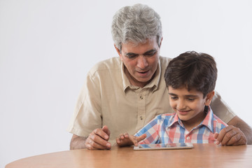 Grandfather and grandson sitting together using digital tablet	