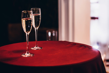 champagne glasses on red table at evening wedding ceremony reception, with lights on background....
