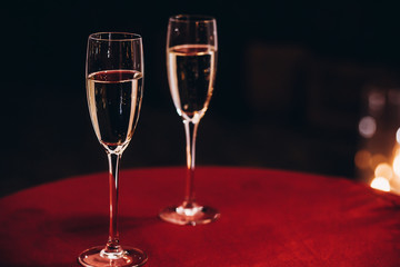 champagne glasses on red table at evening wedding ceremony reception, with lights on background. space for text. christmas new year feast, luxury life celebration