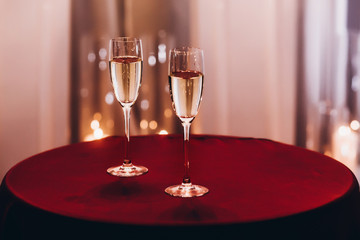 champagne glasses on red table at evening wedding ceremony reception, with lights on background....