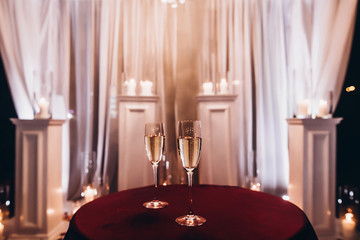 glasses with bubble champagne on red table at evening wedding ceremony reception, with lights in...