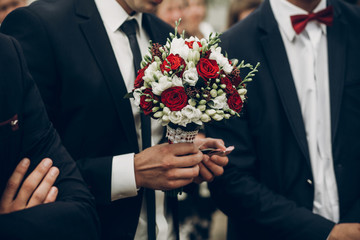 groom holding stylish bouquet of red roses before wedding ceremony for bride
