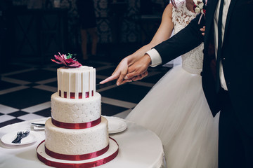 bride and groom cutting wedding cake. wedding couple tasting big delicious cake with pearl and red flower at wedding reception in restaurant. luxury catering