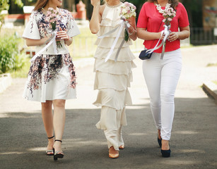Obraz premium bride in vintage dress and bridesmaids with bouquets walking in sunny park at wedding reception