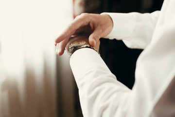 stylish groom dressing up, getting ready in morning for wedding ceremony, putting on golden watch