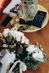 stylish wedding rings bow tie watch and cuff links and bouquets for bride and groom. luxury roses and golden leaves, and man set on wooden table. morning preparation. space for text