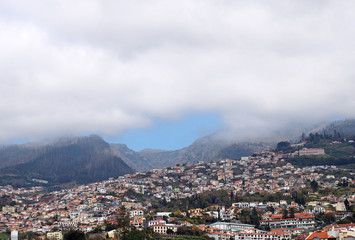 Fototapeta na wymiar a wide panoramic view of the city of funchal in madeira with houses and tree covered hills under a cloudy sky