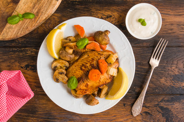 Tilapia fish fillet baked with vegetables, carrot, celery and mushrooms. White plate on wooden rustic table, top view