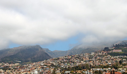 a wide panoramic view of the city of funchal in madeira with houses and tree covered hills under a...