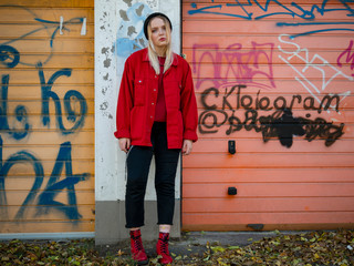 nice girl in a knitted hat, a red jacket and red boots stands near the gate of the garage with...