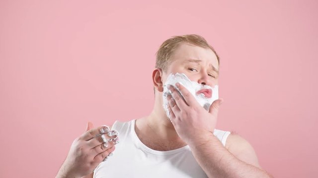 Cropped shot of upset man with gel on cheeks, has sad expression, sensitive skin, man going to shave his chin despite ofskin irritation, isolated over pink background.