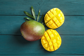 Obraz na płótnie Canvas Cut ripe mangoes and palm leaf on wooden background, space for text