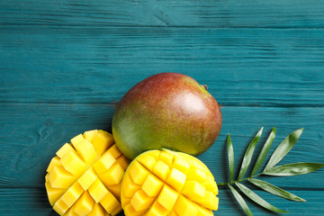 Cut ripe mangoes and palm leaf on wooden background, space for text