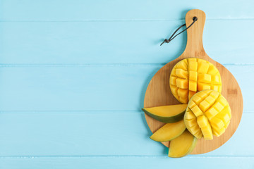 Cutting board with cut ripe mangoes on color background, top view