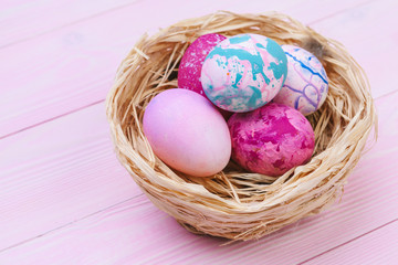 Colorful easter eggs in a nest on pink wooden background