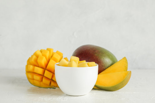 Small bowl with mango pieces and cut mangoes on white background, space for text