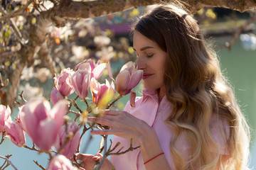 Blonde girl sniffs magnolia buds in the spring garden by the lake © Aleksandr