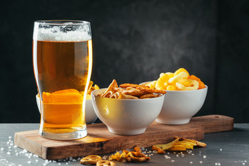 Glass of lager beer with snack bowls on dark stone background