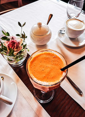 top view fresh carrot  juice in a glass with a straw on the table against the background of cups of coffee and a decorative orchid flower