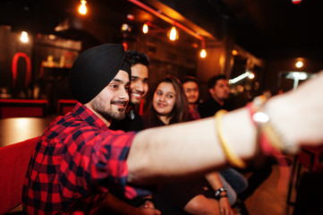 Group of indian friends sitting at lounge bar, having fun and rest, smoking hookah and looking on mobile phones to make selfie.