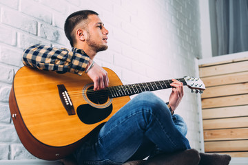 Obraz premium Handsome mature man in casual clothes is smiling while playing guitar at home