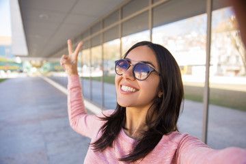 Smiling woman showing victory sign and taking selfie photo 
