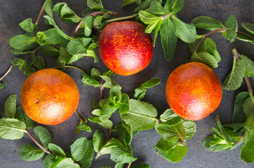 Top view of fresh picked fragrant mint and blod oranges on grey surface