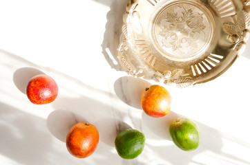 Rustic golden tray with scratches and blood oranges,limes on the white marble table.Sun shades on the the table in the morning
