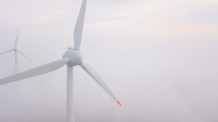 Windmills in the fog at sunrise. Wind turbine from aerial view. Sustainable development, environment friendly.