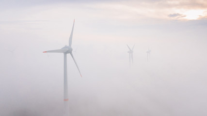 Windmills in the fog at sunrise. Wind turbine from aerial view. Sustainable development, environment friendly.
