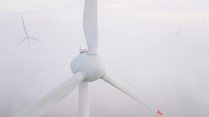 Windmills in the fog at sunrise. Wind turbine from aerial view. Sustainable development,...