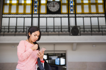 Worried woman using smartphone in station hall