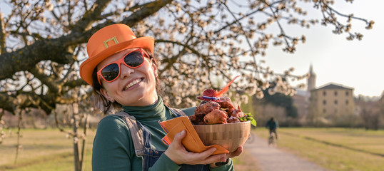 Girl with accessories for the holiday King's Day in the Netherlands, holding a bowl with donuts. Traditional pastries for the festival. Family picnic in the park in spring. Flowering trees 