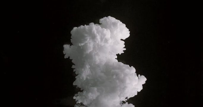 Slow motion of white dye spilling into clear liquid.