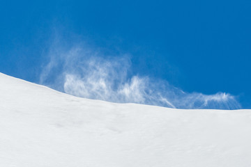 strong gust of wind raising snow in mountains, blue sky