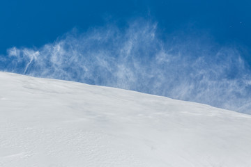 Fototapeta na wymiar strong wind dispersing snow in winter, blue sky