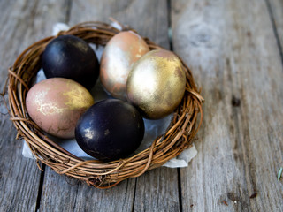 Golden and black eggs in a nest on an old wooden background. Copy space, selective focus, close up. Eggs for Easter. Card.