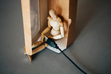 The figurine of a wooden man sitting with charge. Conceptual image about psychological experiences.Wood man in chronic fatigue. Burnout. Fatigue. No energy. Stress symptom.