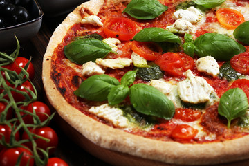 Pizza with tomatoes, mozzarella cheese, black olives and basil. Delicious italian pizza on wooden pizza board.