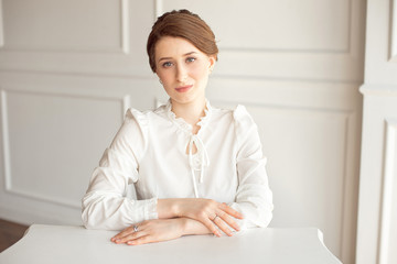 Portrait of a beautiful smiling young brunette businesswoman in a white shirt sitting on a bright...