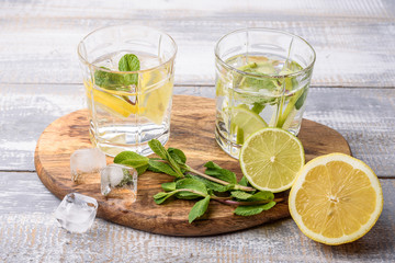 homemade lemonade with lemon, lime, mint and ice cubes on light grey wooden background