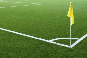 Corner of a football field. White markings on green grass and yellow flag. No people and players. Sports concept.