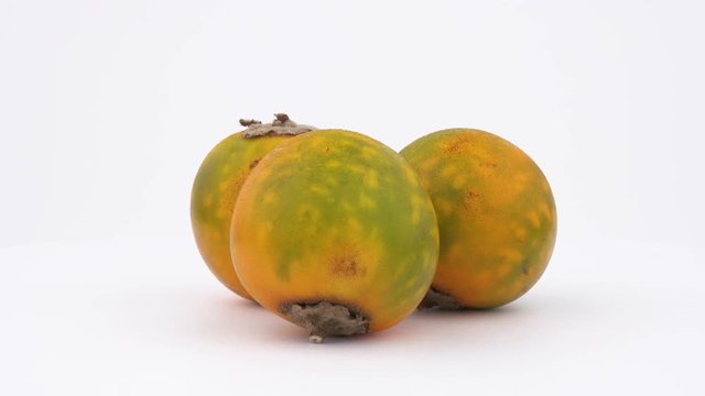 Close-up view of a three naranjilla fruits, rotating on the turntable. Isolated on white background.