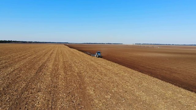Tractor plowing a agricultural field, aerial view - Drone shot of tractor cultivating arable land for seeding crops, gulls flying around